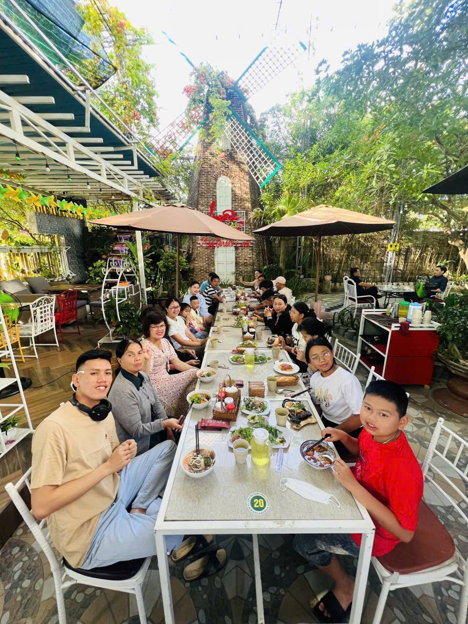 Gia đình nhiều thế hệ ngồi ăn ở bàn dài ngoài sân vườn